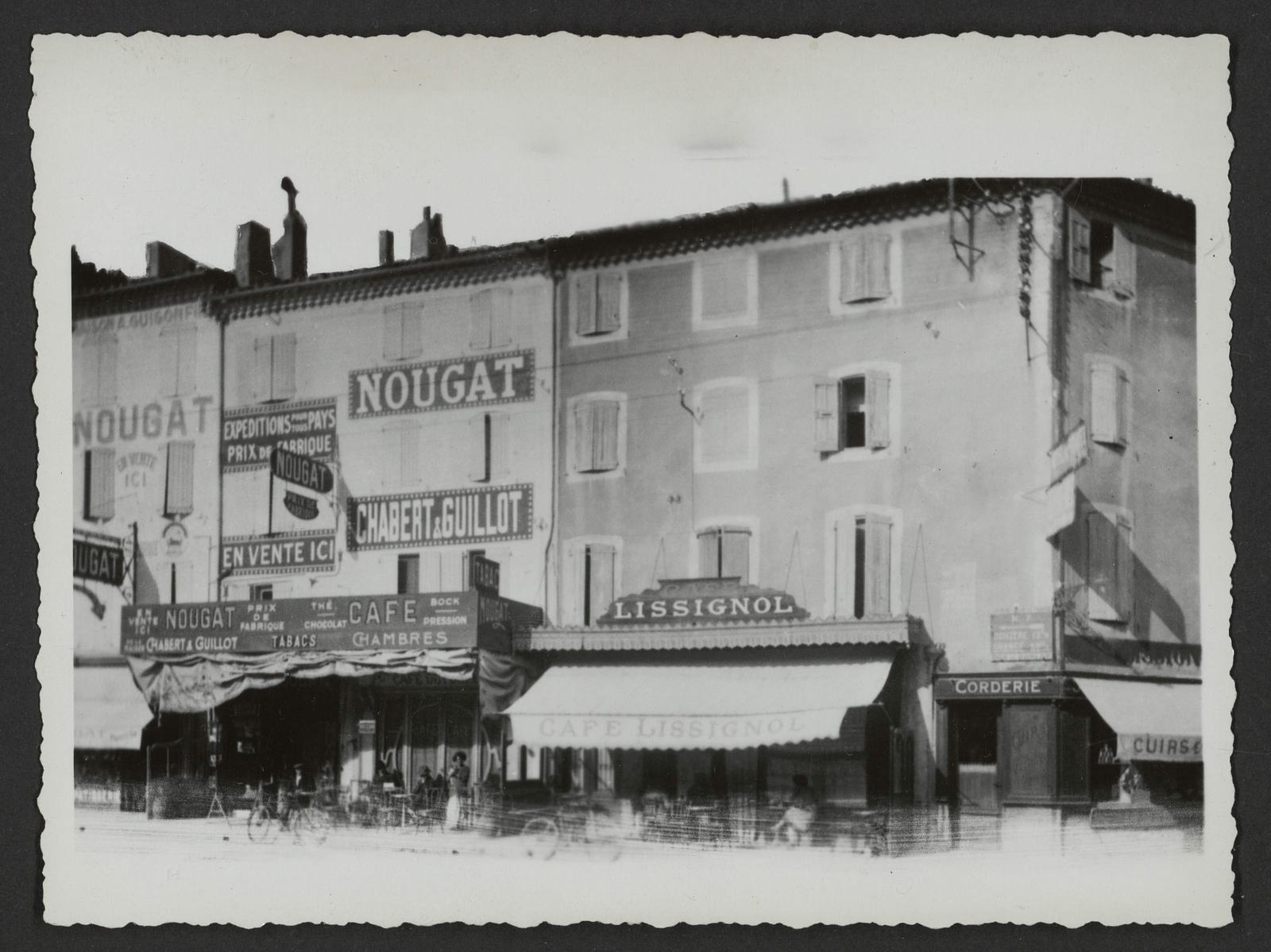 Photographie ancienne d'une rue de Montélimar aux façades couvertes d'enseignes de nougat, dont Chabert et Guillot